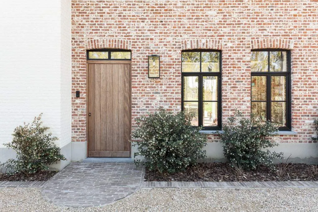 Houten voordeur naast zwarte steellook ramen in rode baksteen
